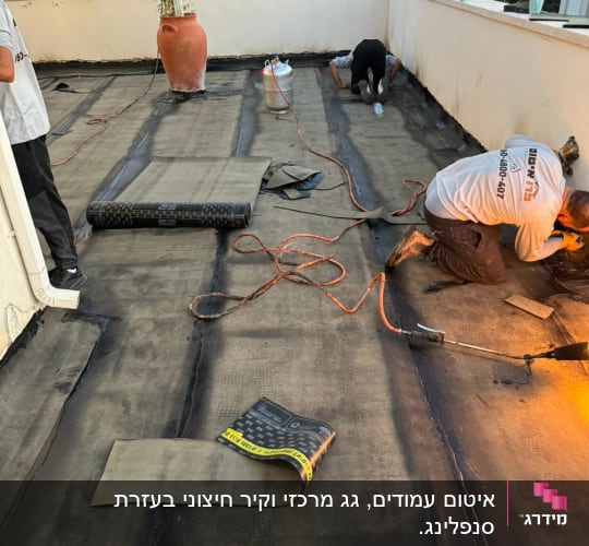 עובדים אוטמים גג עם יריעות ביטומניות ומבער גז.